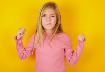 Ein blondes Mädchen in rosa T-Shirt vor einem gelben Hintergrund.
