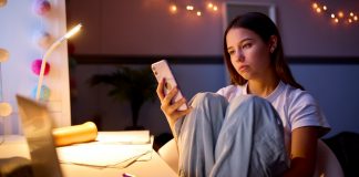 EIn Mädchen mit angezogenen Knien blickt unzufrieden auf ihr Handy.