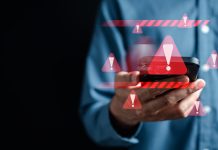 Warnzeicheneinblendungen um ein Handy, das jemand mit einem blauen Hemd vor dunklem Hintergrund in die Kamera hält.