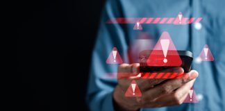 Warnzeicheneinblendungen um ein Handy, das jemand mit einem blauen Hemd vor dunklem Hintergrund in die Kamera hält.