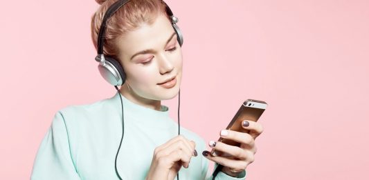 Lächelnde Frau mit Kopfhörern, die auf ihr Handy blickt.