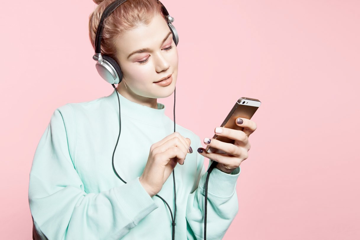 Lächelnde Frau mit Kopfhörern, die auf ihr Handy blickt.