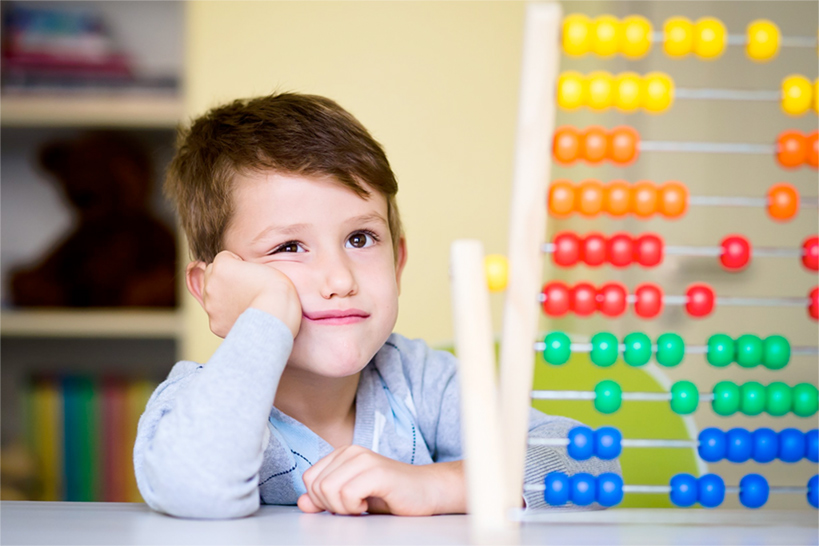 Ein Junge im Grundschul- oder Kindergartenalter schaut skeptisch auf einen Rechenschieber.
