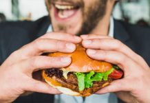 Bärtiger Mann hinter mit beiden Händen erhobenem Hamburger